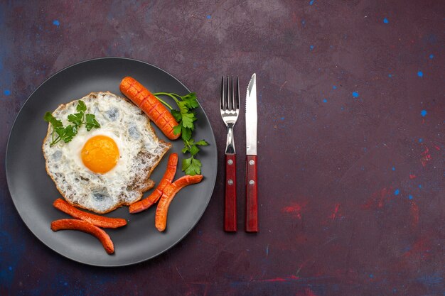 Top view of scrambled eggs with greens and sausages inside plate on dark surface