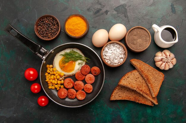 Top view scrambled eggs with sausages and different seasonings on dark green background