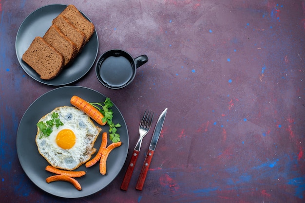 Top view of scrambled eggs with sausages and greens bread loafs tea on the dark surface