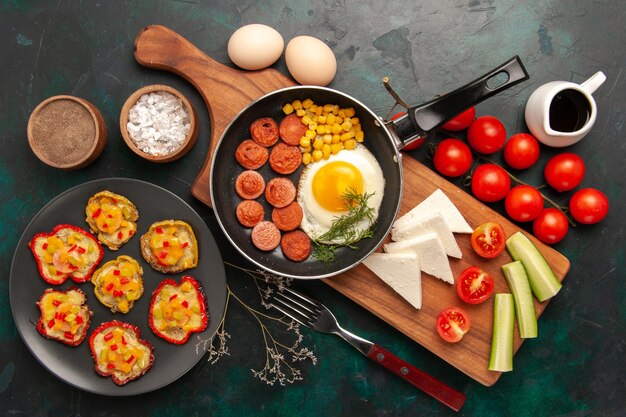 Top view scrambled eggs with sliced sausages fresh tomatoes and raw eggs on dark background