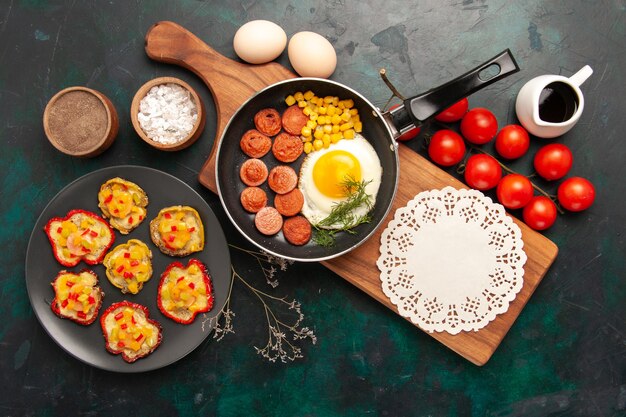 Top view scrambled eggs with sliced sausages and raw eggs on dark background