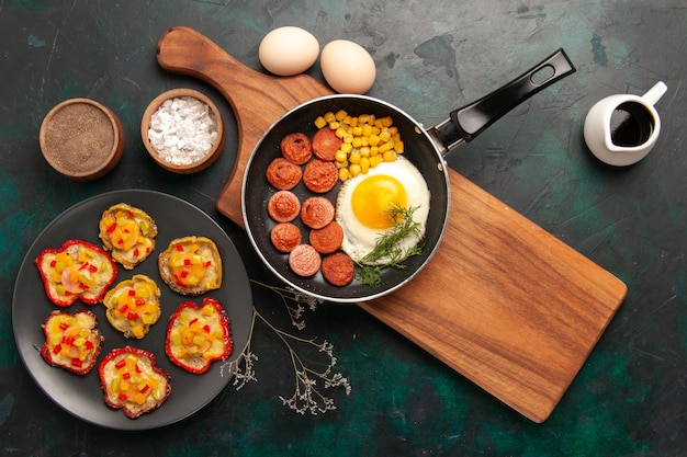 Top view scrambled eggs with sliced sausages and raw eggs on the dark background