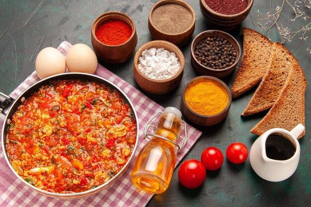 Top view scrambled eggs with tomatoes and different seasonings on dark-green background