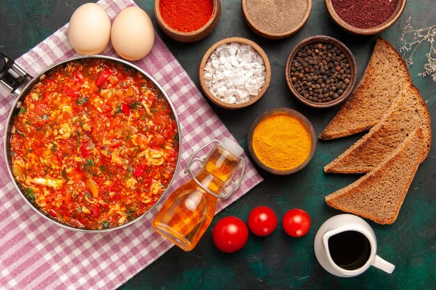 Vista dall'alto uova strapazzate con pomodori e condimenti diversi su sfondo verde scuro