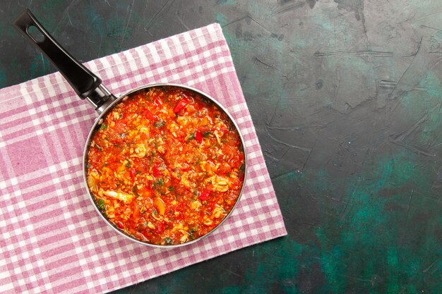 Top view scrambled eggs with tomatoes and greens inside pan on the dark green background