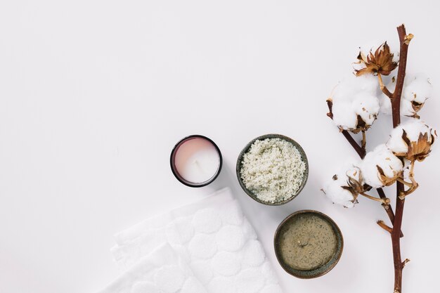 Top view of scrubs; candle; napkin and cotton twig on white surface