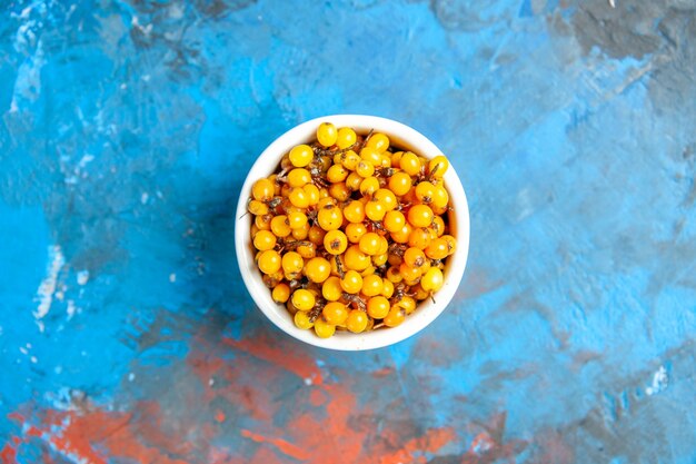 Top view of sea buckthorn in bowl on blue surface