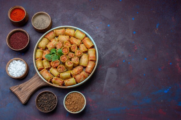 Top view seasonings inside pots salt pepper with meat rolls on the dark-purple surface 