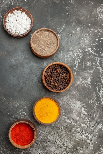 Top view of set of different spices in brown bowls on gray background