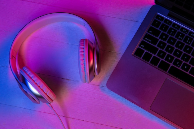 紫色のネオンライトとピンクの背景のガジェットのセットの上面図。ノートパソコンのキーボード、ヘッドフォン、黒い画面のスマートフォン。広告用のコピースペース。テクノロジー、モダン、ガジェット。