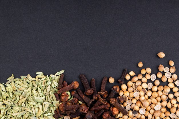 Top view of a set of spices and herbs peppercorns anise seeds and clove on black background with copy space