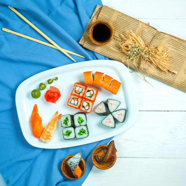 Top view of set of sushi and maki with soy sauce on blue and white