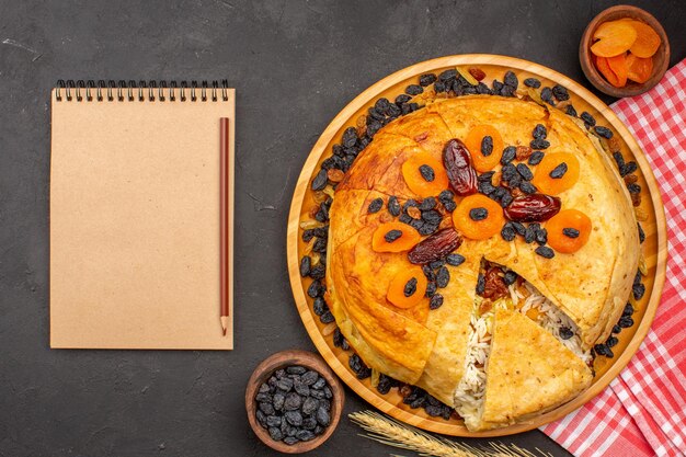 Top view of shakh plov delicious rice meal cooked inside round dough with raisins and notepad on grey surface