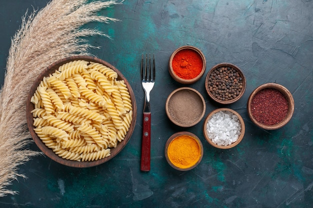 Top view shaped italian pasta with different seasonings on dark blue background