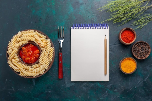 Free photo top view shaped italian pasta with notepad and different seasonings on dark blue background