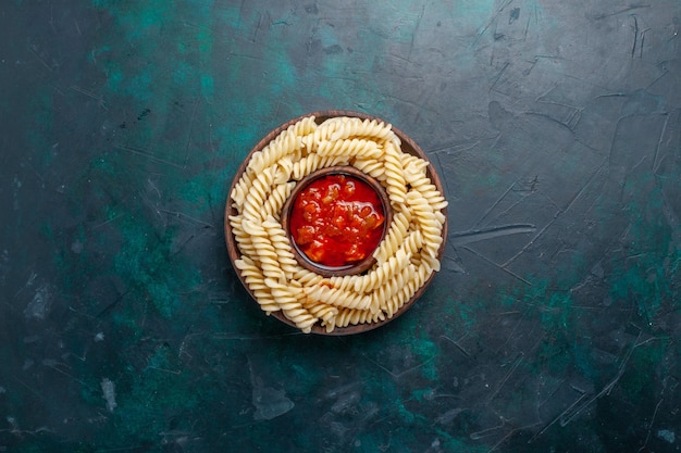 Top view shaped italian pasta with tomato sauce on dark-blue desk