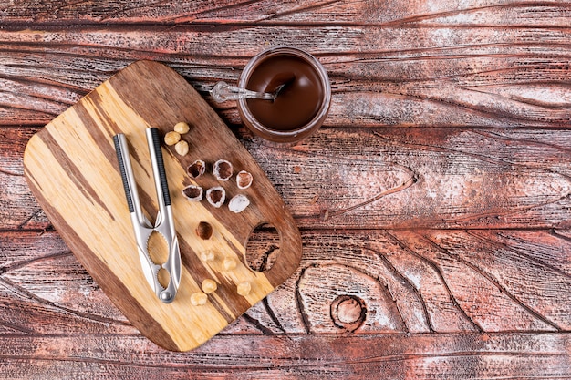 Top view shelled and cleaned hazelnuts with cocoa spread and nutcrackers on wooden table.