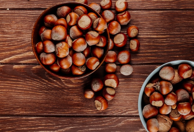 Top view of shelled hazelnuts in bowls on dark wooden rustic background