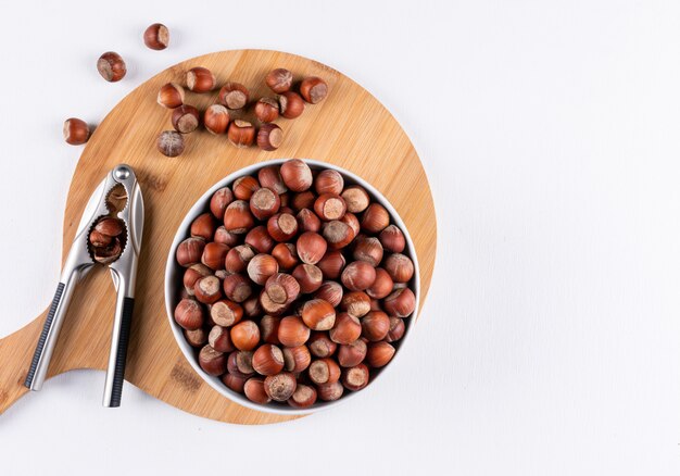 Top view shelled hazelnuts in white bowls with nutcracker on wooden cutting board