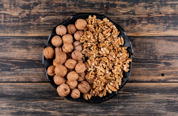 Top view shelled and raw walnuts in black plate on wooden  horizontal