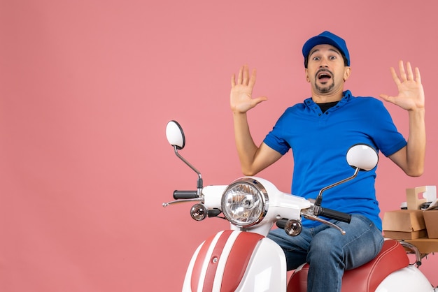 Top view of shocked courier guy wearing hat sitting on scooter delivering orders on pastel peach background