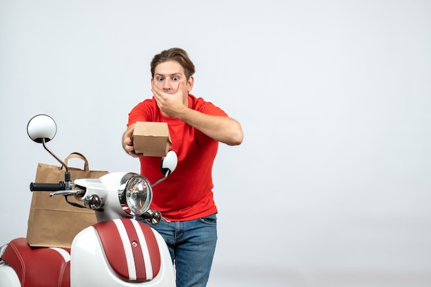 Top view of shocked delivery guy in red uniform standing near scooter giving order on white background