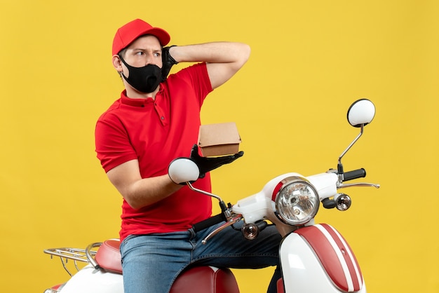 Top view of shocked delivery guy wearing red blouse and hat gloves in medical mask sitting on scooter showing order