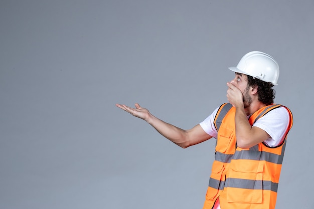 Top view of shocked male architect in warning vest with safety helmet and pointing up on the right side on gray wave wall