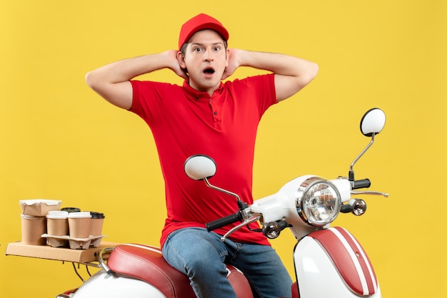 Вид сверху шокированного молодого человека в красной блузке и шляпе, доставляющего заказ, сидя на скутере на желтом фоне