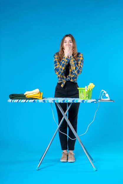 Top view of shocked young girl standing behind the ironing board and posing