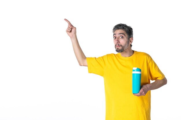 Top view of shocked young male in yellow shirt and showing blue thermos pointing up on white surface