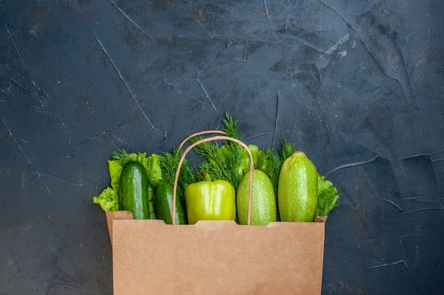 Top view shopping bag cucumbers bell pepper zucchini lettuce dill on black table
