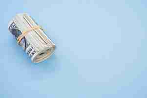 Free photo top view shot of a bundle of rolled-up american banknotes isolated on a light blue background