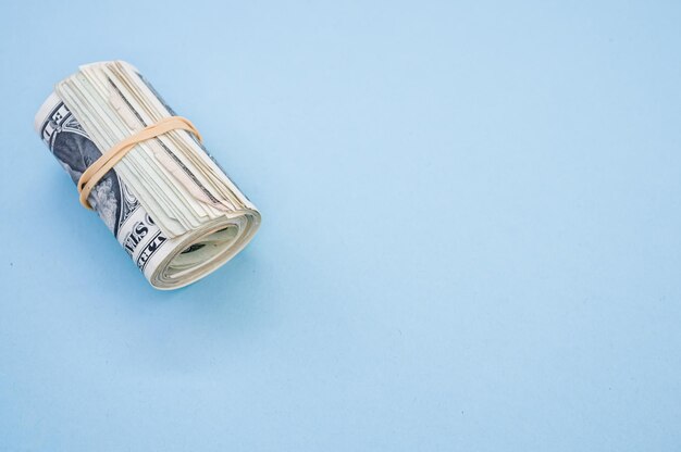 Top view shot of a bundle of rolled-up American banknotes isolated on a light blue background