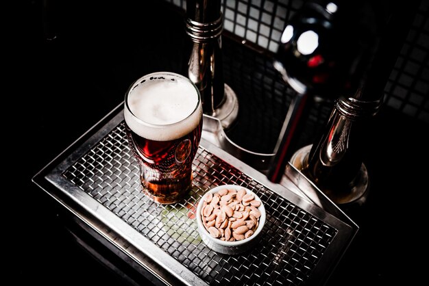 Top view shot of a glass of lager beer with a cup of peanuts on a metal screen tray