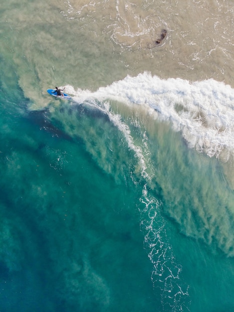 Top view shot of a person with a surfboard swimming in Varkala Beach