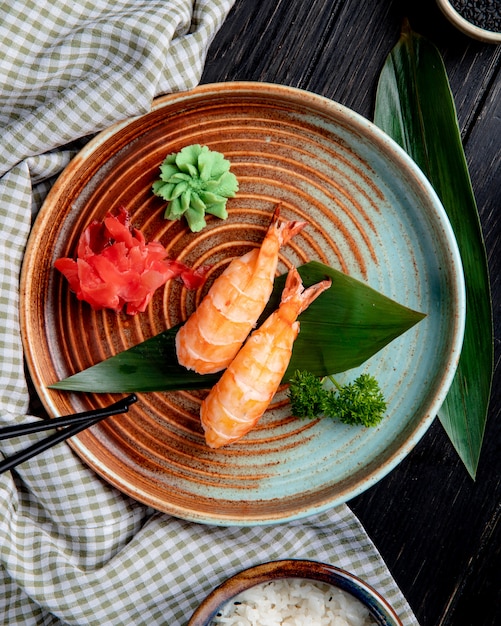 top view of shrimp nigiri sushi on bamboo leaf served with pickled ginger slices and wasabi on a plate