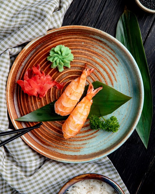 top view of shrimp nigiri sushi on bamboo leaf served with pickled ginger slices and wasabi on a plate