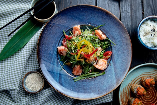 Top view of shrimp salad with bell peppers and arugula on a plate on wood