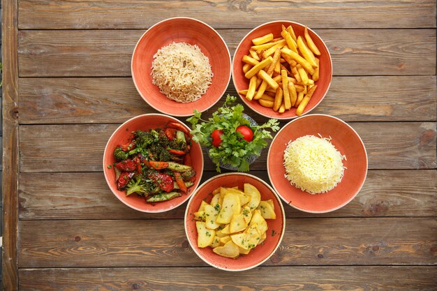 Top view of side dish bowls with fried potatoes, rice and boiled vegetables