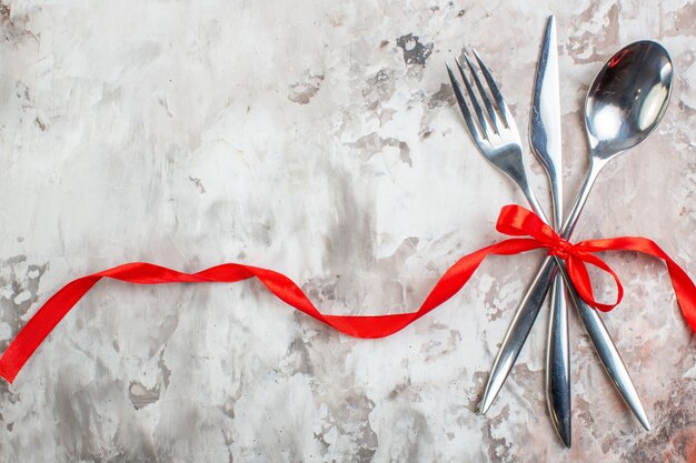 Top view silver cutlery with red bow on light surface