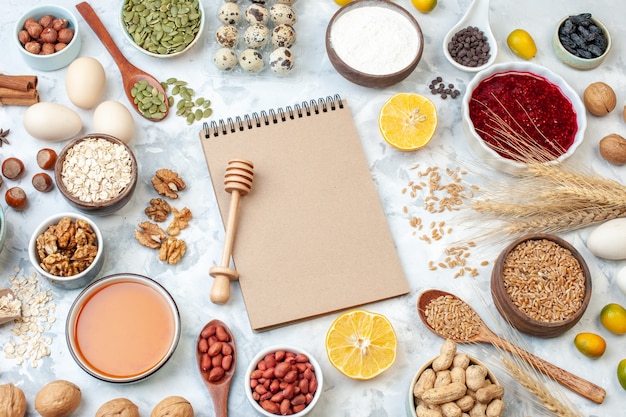 Top view simple notepad with eggs flour jelly different nuts and seeds on a white nut color cake sweet pie photo sugar dough fruit