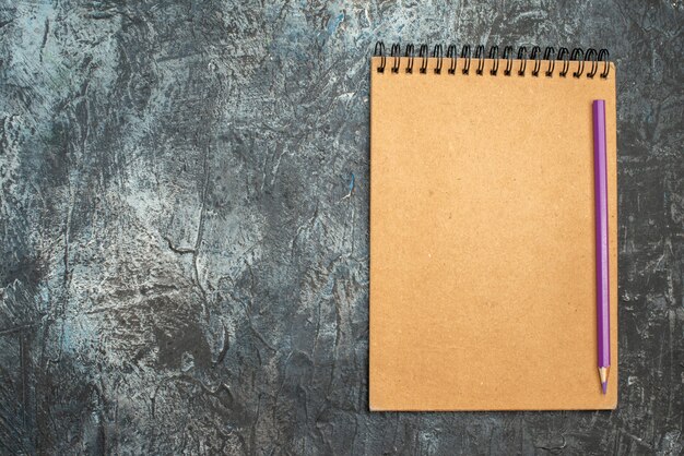 Top view of simple notepad with pencil on grey surface