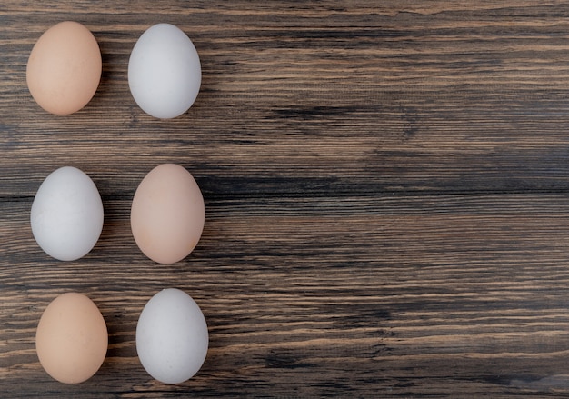Top view of six chicken eggs arranged on a wooden background with copy space