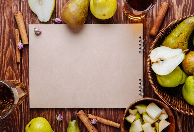 Top view of a sketchbook and fresh ripe pears with a glass of pear juice on wooden background