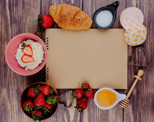Вид сверху альбом и свежей спелой клубники с медом, сахаром, круассаном, творогом и печеньем по дереву