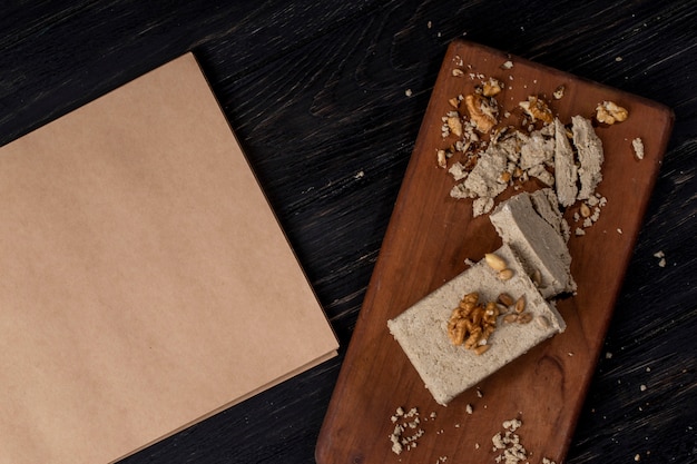 Top view of sketchbook and halva with sunflower seeds and walnuts on a wooden board