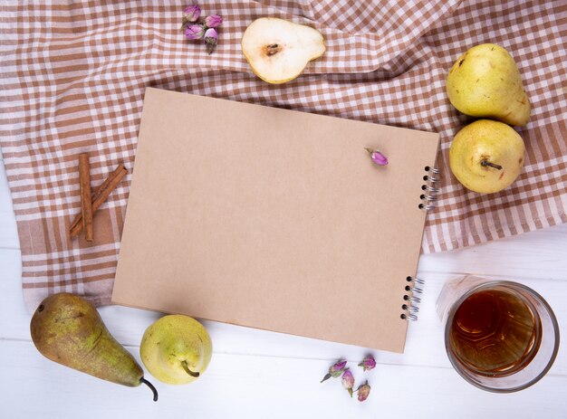 Top view of sketchbook made of craft paper with fresh ripe pears and a glass of lemonade on plaid tablecloth