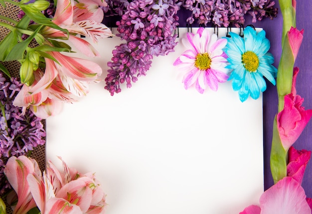 Top view of a sketchbook and pink and purple color flowers gerbera lilac alstroemeria and daisy flowers on sackcloth on purple wooden background