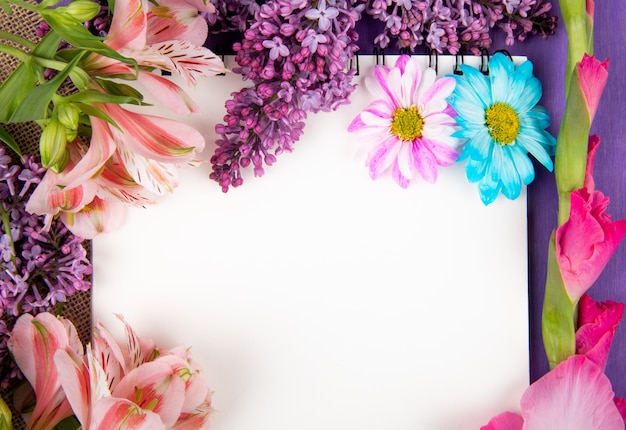 木製の背景が紫色の荒布を着たスケッチブックとピンクと紫の色の花ガーベラライラックアルストロメリアとデイジーの花のトップビュー